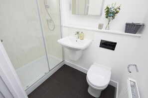 Baño con ducha, lavamanos, inodoro y un pequeño estante con artículos de aseo.
