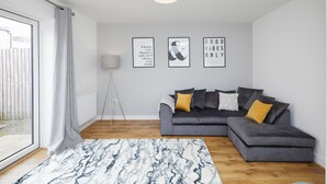 A modern living room with a grey sectional sofa, a marble-patterned rug, and three framed motivational posters on the wall. - 3 Bedroom Large House - Train Station (Derby)