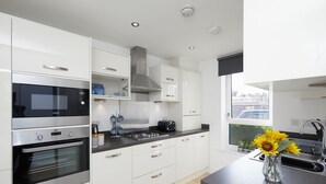 A modern kitchen with white cabinetry, stainless steel appliances, and a large window providing a view of the city. - 3 Bedroom Large House - Train Station (Derby)