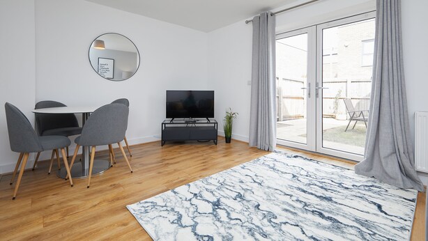 A modern living room with a dining area, a flat-screen TV, and a large sliding glass door to an outdoor patio. - 3 Bedroom Large House - Train Station (Derby)