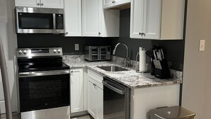 A modern kitchen with white cabinets, stainless steel appliances, a granite countertop, and a stainless steel trash can.