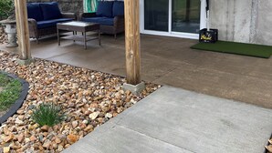 A covered outdoor patio with a concrete floor, stone edging, and a wooden deck above.