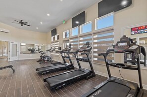 A gym with treadmills, stationary bikes, and a ceiling fan.