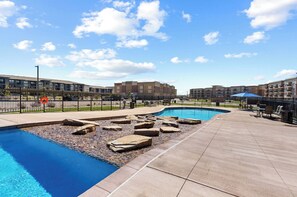 A pool area with two pools, a patio, and a fence.