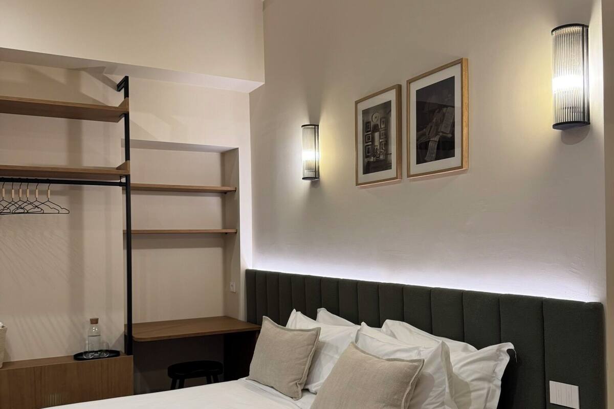 A modern bedroom with a bed, a wooden nightstand, a built-in wardrobe, and two wall-mounted light fixtures.