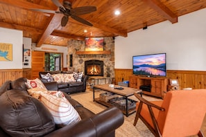 A cozy living room with a stone fireplace, leather sofa, and a television. - Lake Winnipesaukee | Pet Friendly | Fire Pit (Gilford)