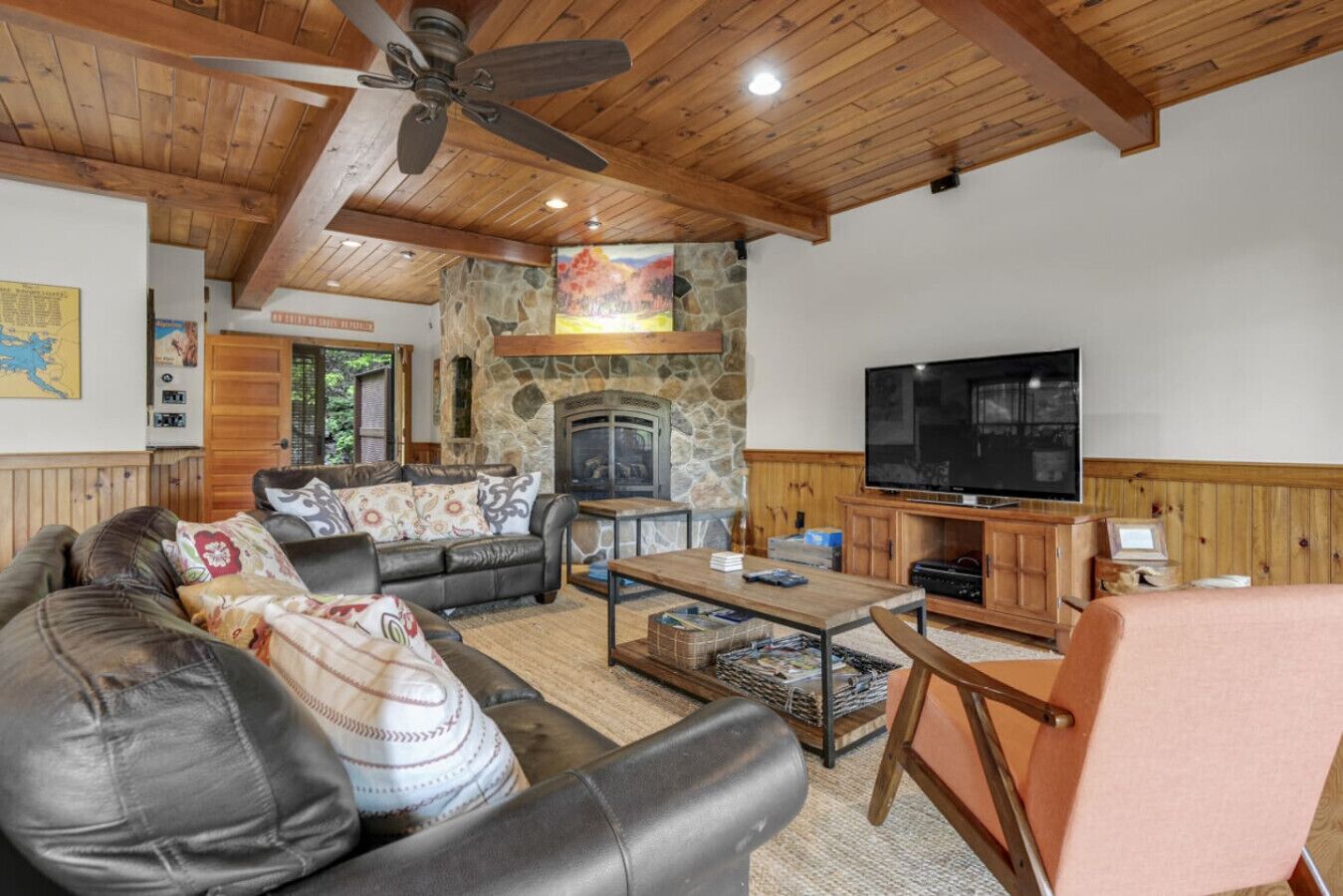 A cozy living room with a stone fireplace, leather sofa, and a television on a wooden cabinet.