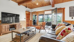 A cozy living room with a large TV, wooden furniture, and a view of the outdoors. - Luxury Lake Retreat | Game Room | Winnipesaukee (Gilford)