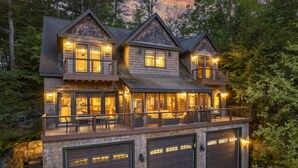 A multi-story house with a stone foundation, large windows, and a balcony with outdoor seating. - Luxury Lake Retreat | Game Room | Winnipesaukee (Gilford)