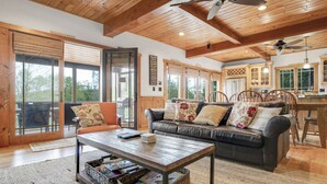 A spacious living room with a wooden ceiling, a sofa, a coffee table, and a dining area with a kitchen in the background. - Luxury Lake Retreat | Game Room | Winnipesaukee (Gilford)