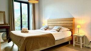 A neatly made bed with a wooden headboard, two bedside lamps, and a window with curtains. - Terrasse Felix Faure (Niza)