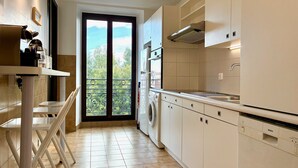 A modern kitchen with a built-in washing machine, a sink, and a window with a view of greenery. - Terrasse Felix Faure (Niza)