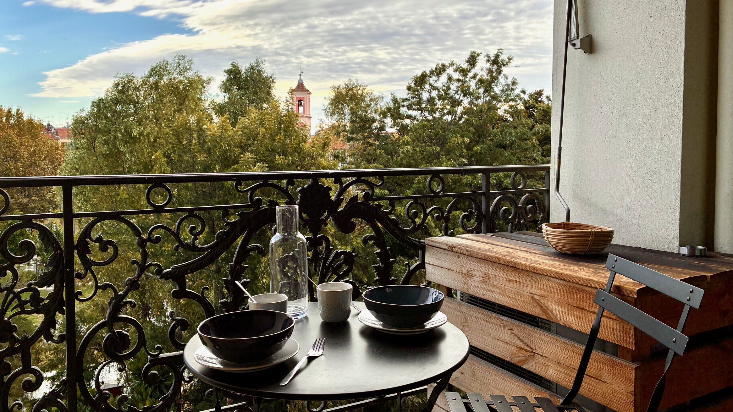 A balcony with a round table, two bowls, a bottle, and a cup.