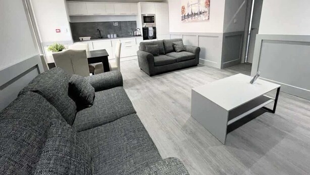 Ein modernes Wohnzimmer mit grauem Sofa, einem weißen Couchtisch und einer Küche im Hintergrund.