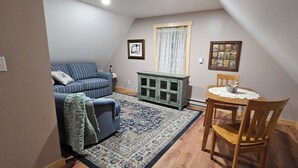 Un salon chaleureux avec un canapé à rayures bleues, un meuble vert, un tapis à motifs et une table à manger en bois accompagnée d’une chaise.