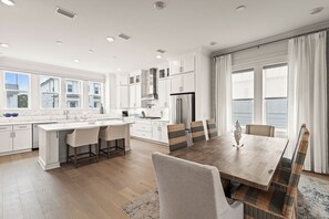 Een moderne keuken met witte kastjes, een centraal eiland en een eethoek met een houten tafel en rieten stoelen.