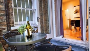 A glass table with a wine bottle and glasses outside a door, leading to a room with a wooden floor and chairs. - *NEW* Notting Hill - It's The One One One! (2) (London)