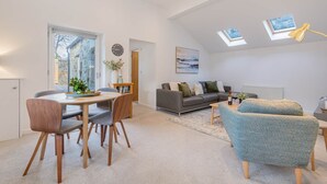 A modern living room with a dining area, a grey sofa, a blue armchair, and skylights. - The Old Weigh House -Kirkby Lonsdale (Kirkby Lonsdale)