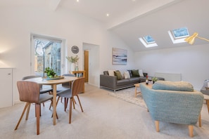 A modern living room with a dining area, a grey sofa, a blue armchair, and skylights.