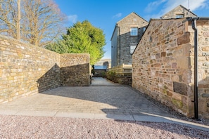 A narrow cobblestone alleyway flanked by stone walls, leading to a stone building with a pitched roof.