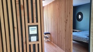 Ein modernes Zimmer mit Holzlamellen, einem Bett, einem kleinen Tisch und einer wandmontierten Bedienkonsole.