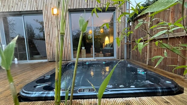 Ein Whirlpool in einem Garten mit einer Holzterrasse und einem modernen Haus im Hintergrund.