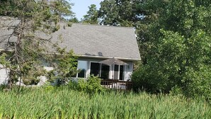 A house with a covered porch, surrounded by tall grass and trees. - Private cabin with resort amenities; kayak, paddleboard, pontoon, great swimming (Pillager)