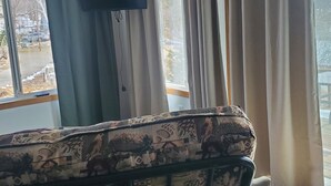A room with a sofa, a television mounted on the wall, and a window with curtains. - Private cabin with resort amenities; kayak, paddleboard, pontoon, great swimming (Pillager)
