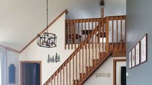 A dining area with a wooden table and chairs, a staircase with wooden railings, and a hanging light fixture. - Private cabin with resort amenities; kayak, paddleboard, pontoon, great swimming (Pillager)