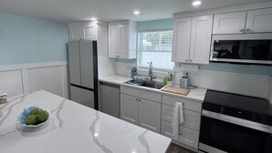 A modern kitchen with white cabinets, a stainless steel refrigerator, a microwave, and a large island with a bowl of fruit. - "The Salty Lime"  Walk to Restaurant/bars, park. (Port Richey)