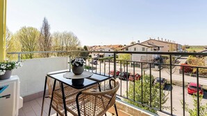 A balcony with a table and chairs, a potted plant, and a view of a residential area with parked cars and houses. - Venice Home perfect for Venice Airport free parking (Veneto)