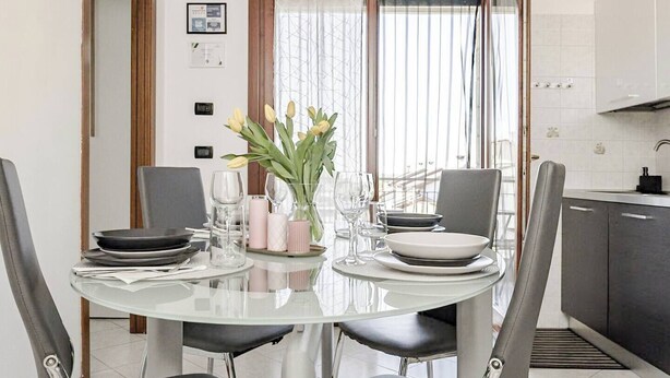 A dining area with a round table, four chairs, a vase with flowers, and a view of the kitchen. - Venice Home perfect for Venice Airport free parking (Veneto)