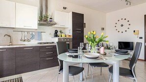 A modern kitchen with dark cabinets, a stainless steel range hood, and a dining area with a glass table and chairs. - Venice Home perfect for Venice Airport free parking (Veneto)