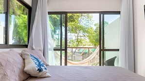 Ein Schlafzimmer mit einem großen Bett, Blick auf einen Garten durch eine Schiebetür und einer Hängematte davor.