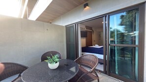 A modern room with a bed, a small table with a potted plant, and a sliding glass door leading to an outdoor area. - Green Porto Residence (Ipojuca)
