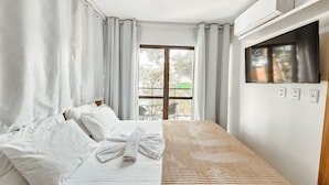 Ein Hotelzimmer mit einem Bett, einem Fenster mit Vorhängen, Blick nach draußen und einer Klimaanlage an der Wand.