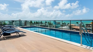 Ein Dachpool mit klarem, blauem Wasser, einer Glasreling und Blick auf das Meer und die Gebäude.