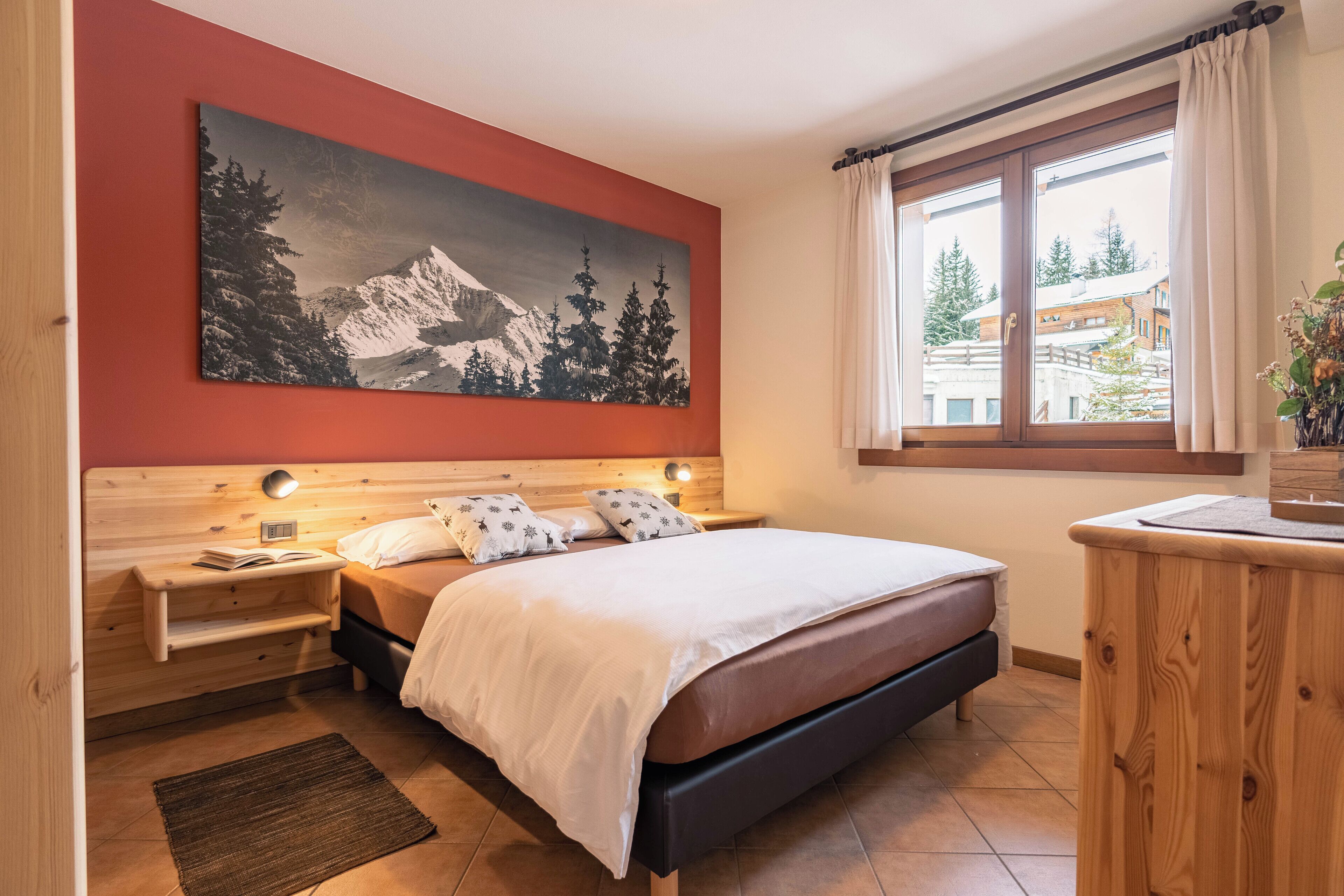 Ein Schlafzimmer mit einem Bett, Nachttischen, einem aufgehängten Gemälde, einem Fenster mit Vorhängen und Blick auf Gebäude.