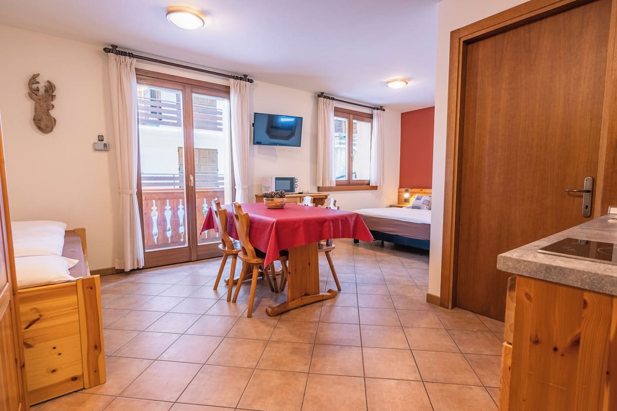 Una habitación acogedora con una cama de madera, una mesa de comedor con sillas, un televisor montado en la pared y una puerta de madera.