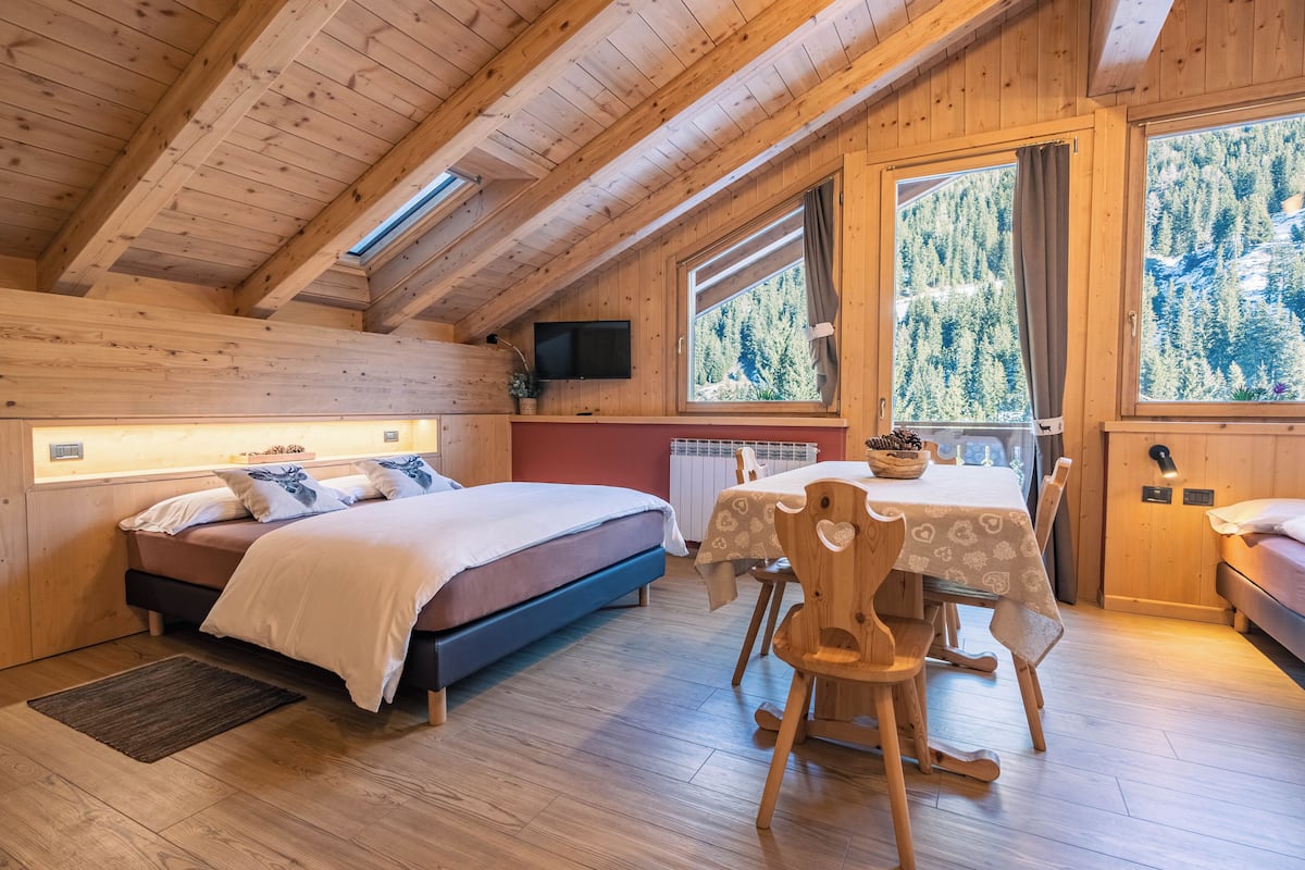 Interior de una cabaña de madera con una cama, una mesa de comedor y un televisor montado en la pared.