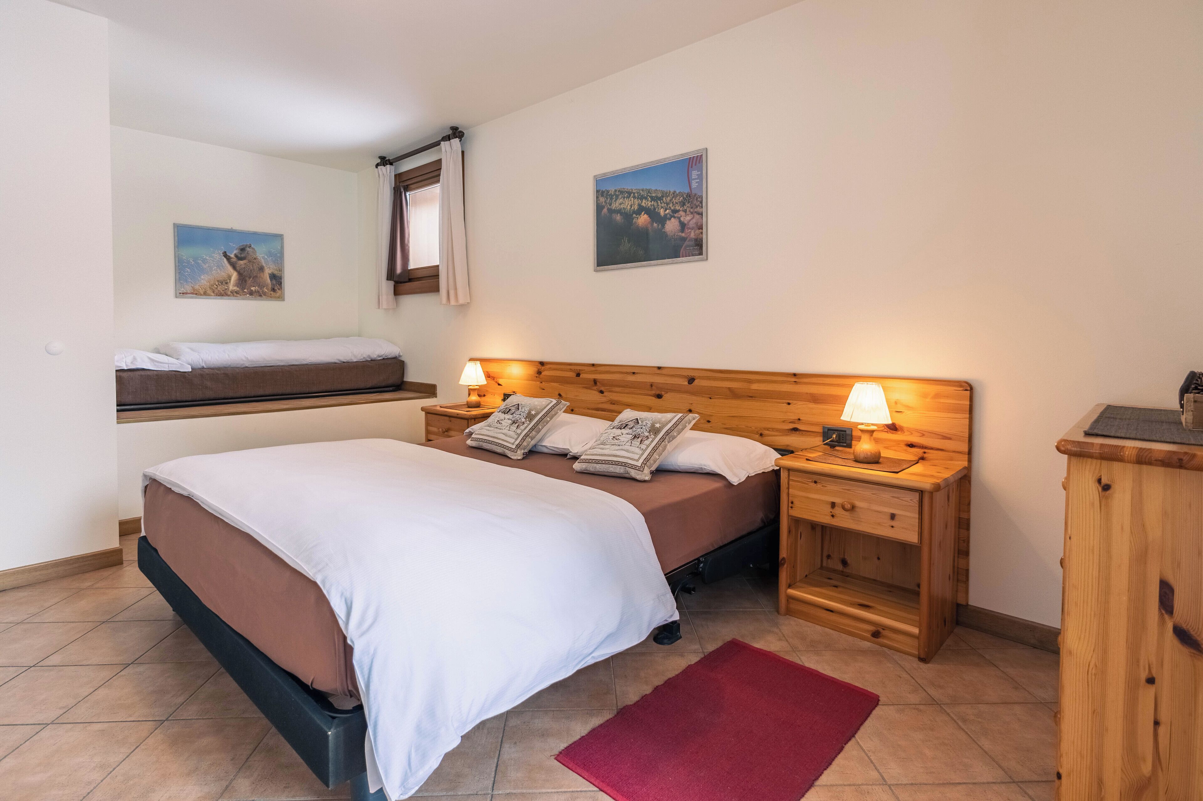 Ein Schlafzimmer mit einem Bett, zwei Nachttischen mit Lampen, einem Holz-Kopfteil, einem roten Teppich und zwei an der Wand befestigten Bildern.