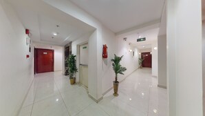 A clean, well-lit hallway with white walls, a marble floor, and potted plants.