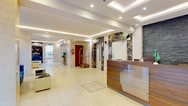 A hotel reception area with a marble wall, a reception desk, a coffee machine, and a blue chair.