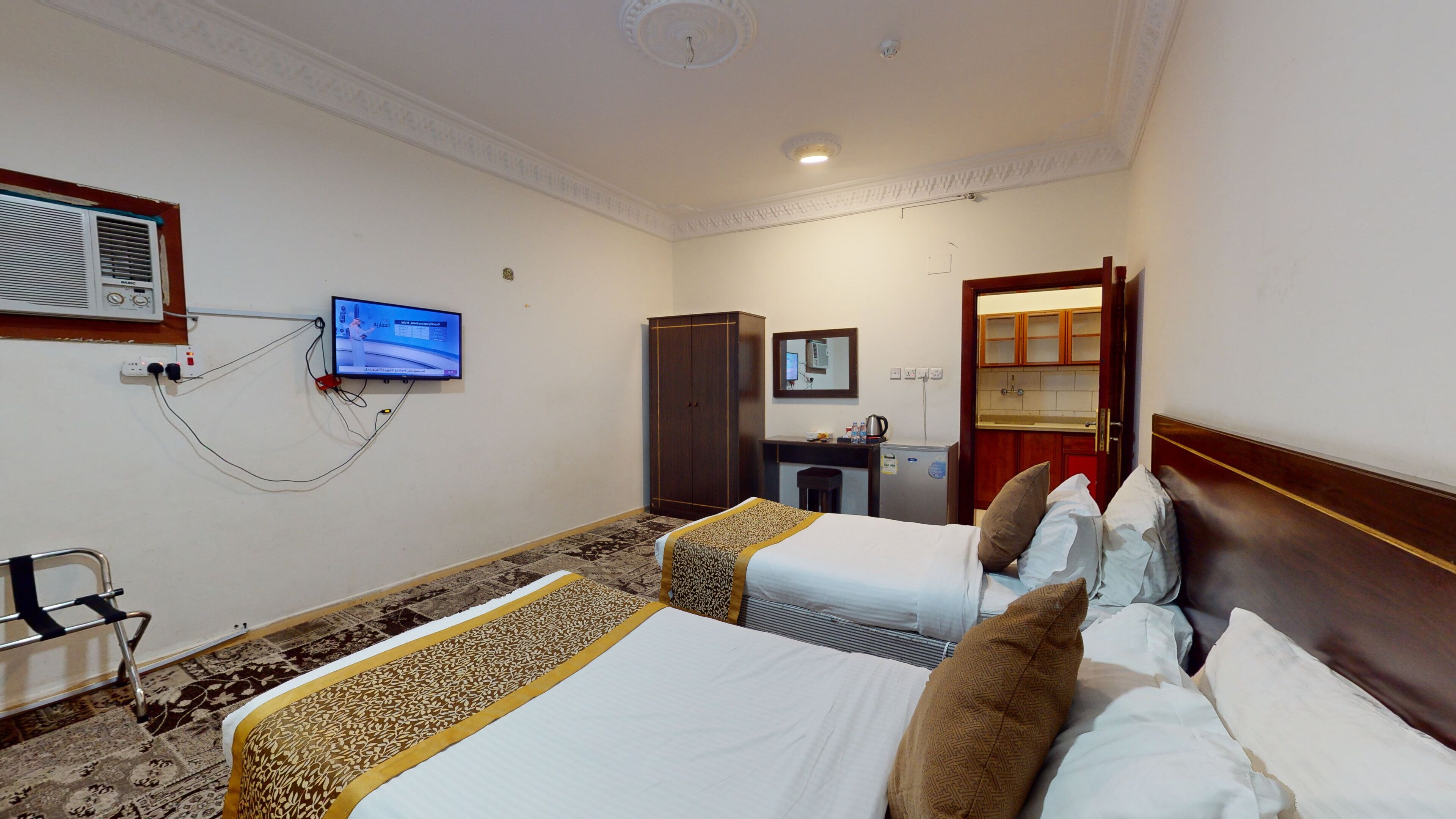 Una camera d'albergo con due letti, una scrivania, un armadio, una televisione e un bagno visibile attraverso una porta aperta.