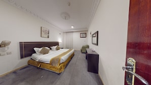 A hotel room with a large bed, a desk, a chair, and a wardrobe.