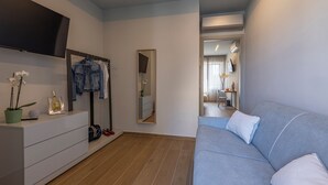 A modern room with a grey sofa, a white dresser, a mirror, and a television mounted on the wall. - Luci sul Mare (Follonica)