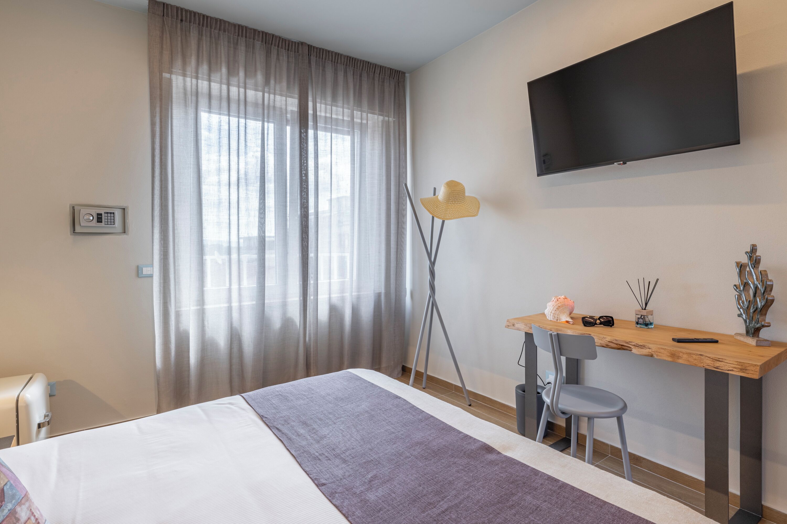 Een hotelkamer met een bed, een bureau, een stoel, een televisie en een raam met gordijnen.