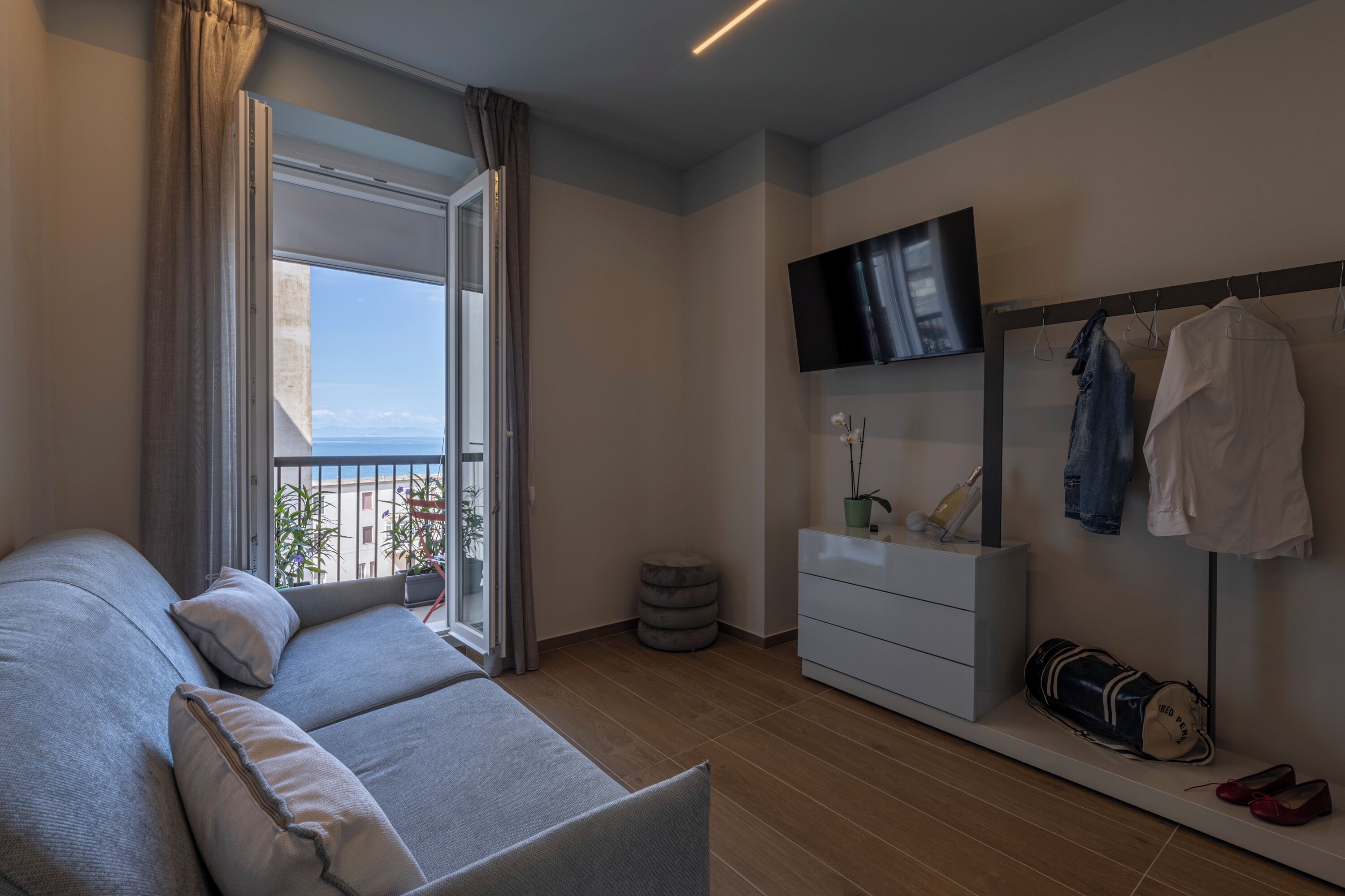 Ein modernes Hotelzimmer mit Sofa, Fernseher, Kleiderschrank und einem Balkon mit Blick.