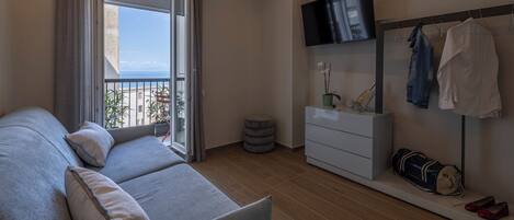 Ein modernes Hotelzimmer mit Sofa, Fernseher, Kleiderschrank und einem Balkon mit Blick.