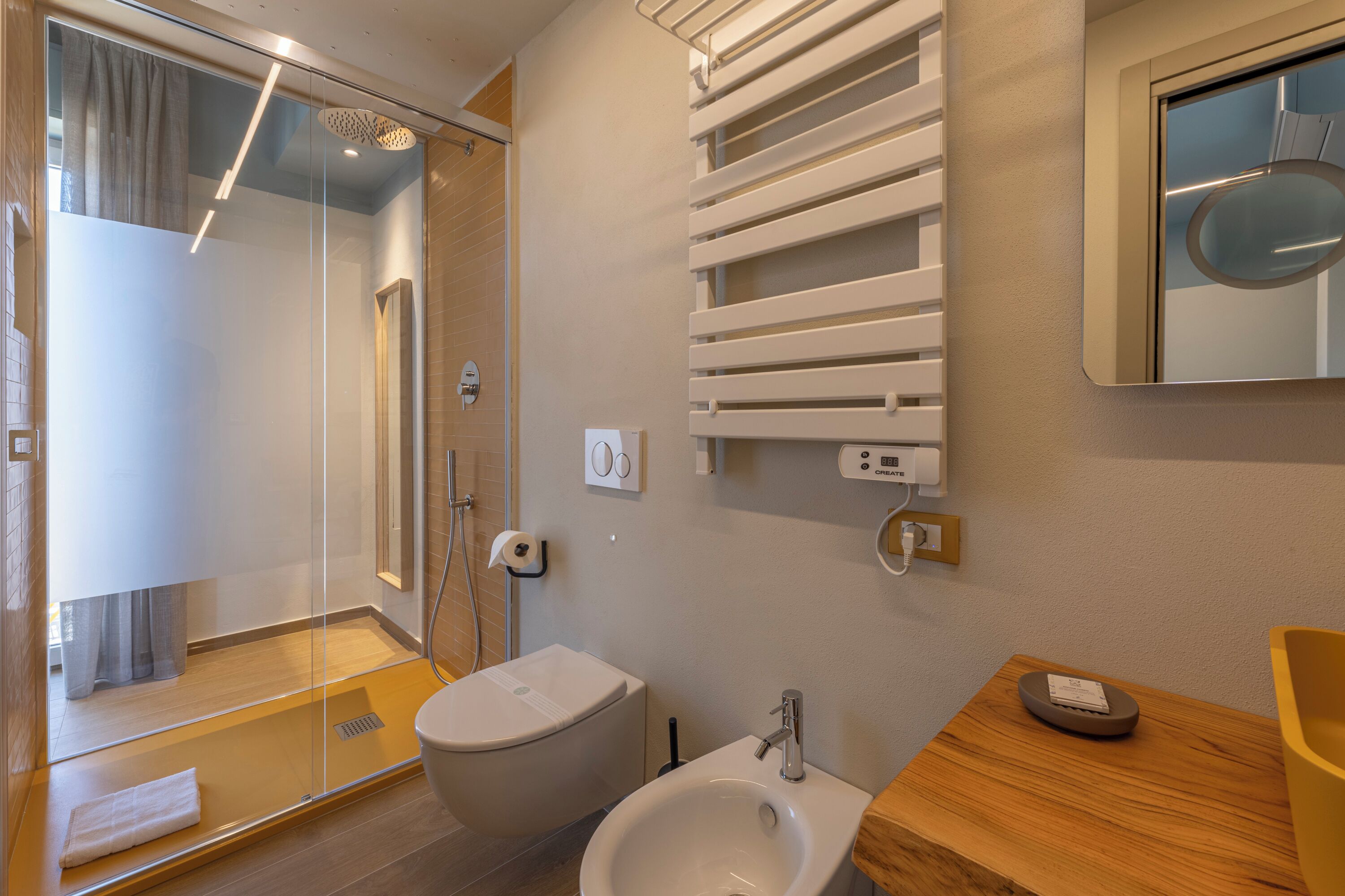 Un baño moderno con cabina de ducha de vidrio, inodoro, bidé y tocador de madera con espejo.